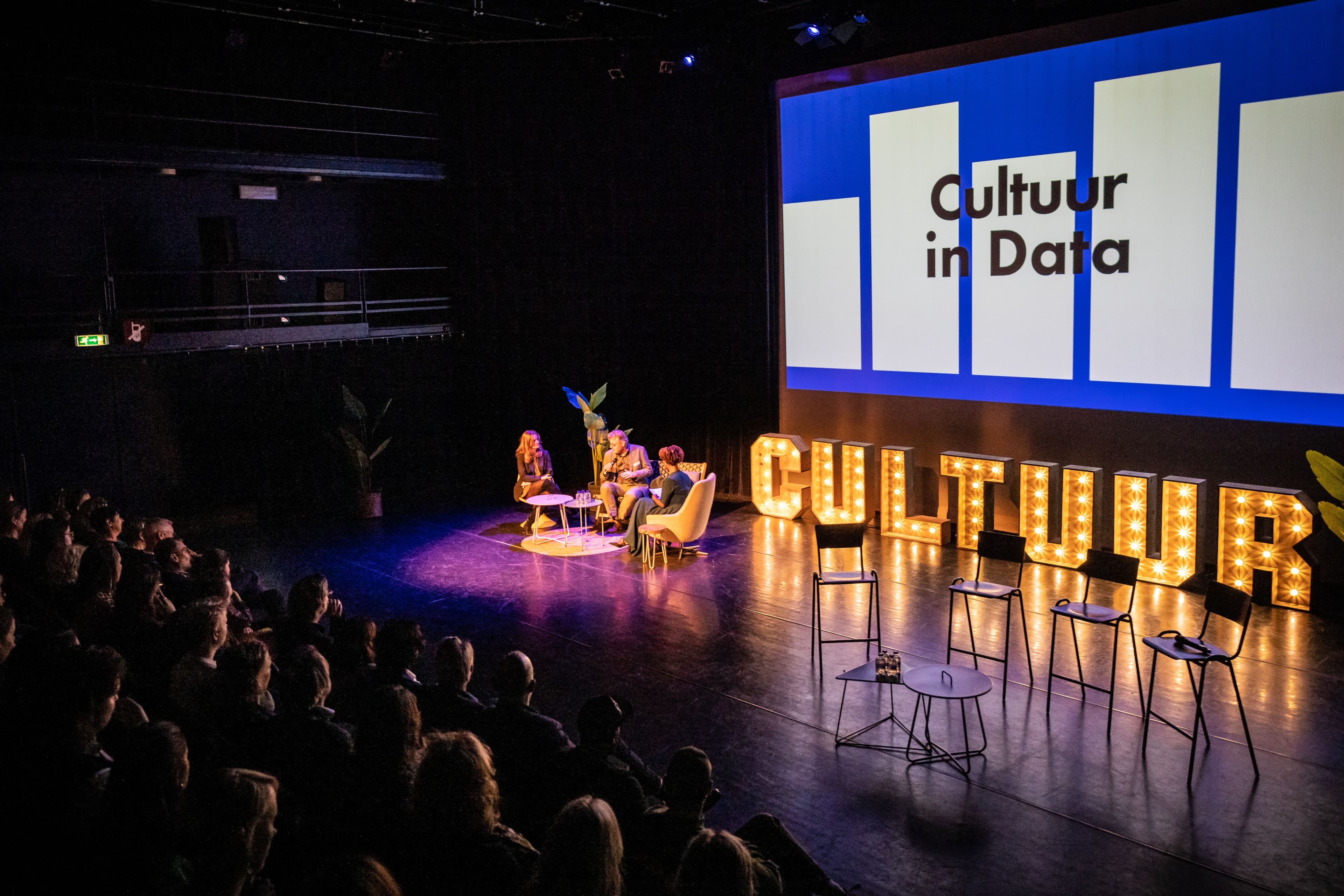 Mensen op een podium met lichtgevende letters die cultuur spellen