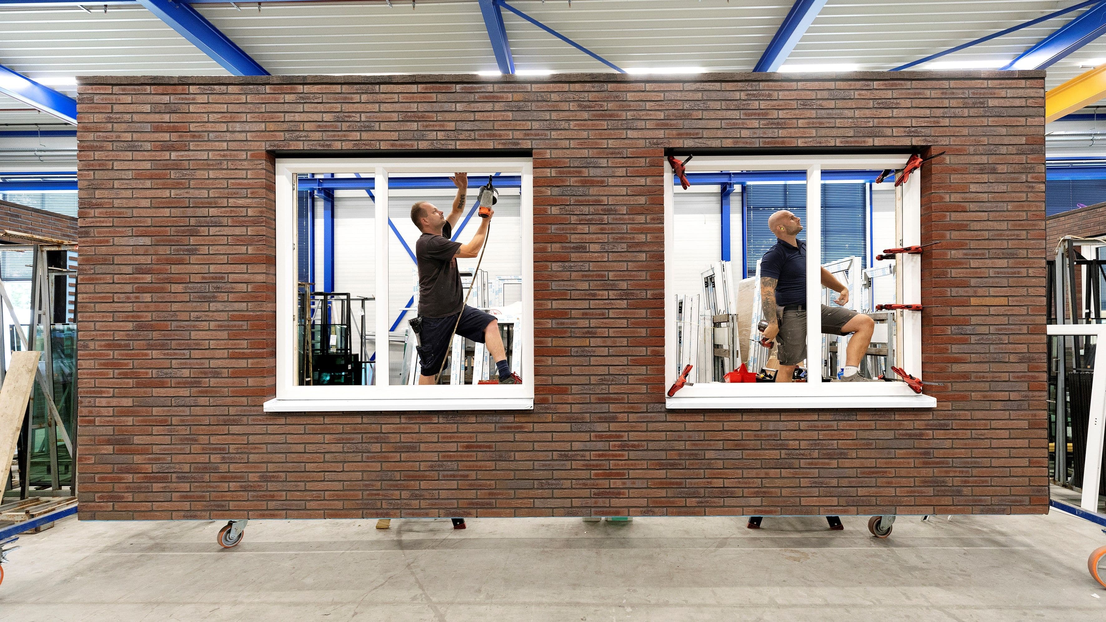 Stenen wand op wielen met 2 mannen die kozijnen plaatsen